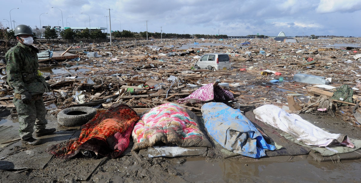 A Japanese soldier stands next to a line of wrapped-up bodies recovered from the sea of devastation and debris in Natori, Miyagi prefecture on March 16, 2011 after the March 11 earthquake and tsunami