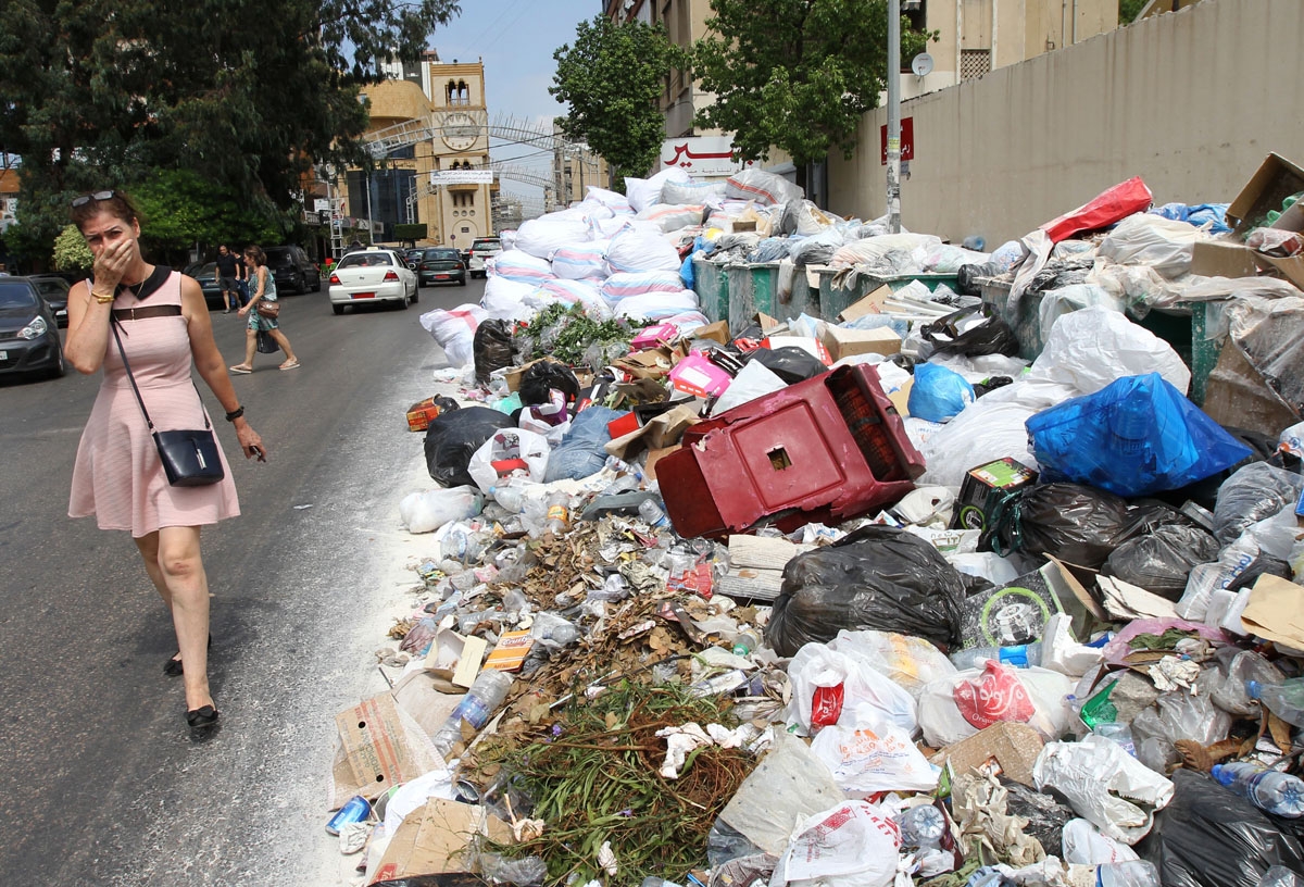 A woman holds her breath as she walks near a temporary garbage dump in the neighbourhood of Jdeideh, northeast of the Lebanese capital Beirut on September 1, 2016