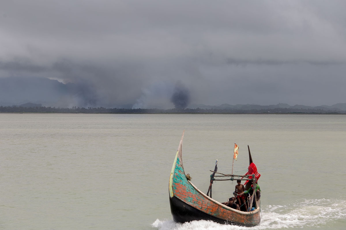 This photograph taken on September 12, 2017 shows Rohingya refugees arriving by boat, as smoke rises from fires on the shoreline behind them, at Shah Parir Dwip on the Bangladesh side of the Naf River after fleeing violence in Myanmar.