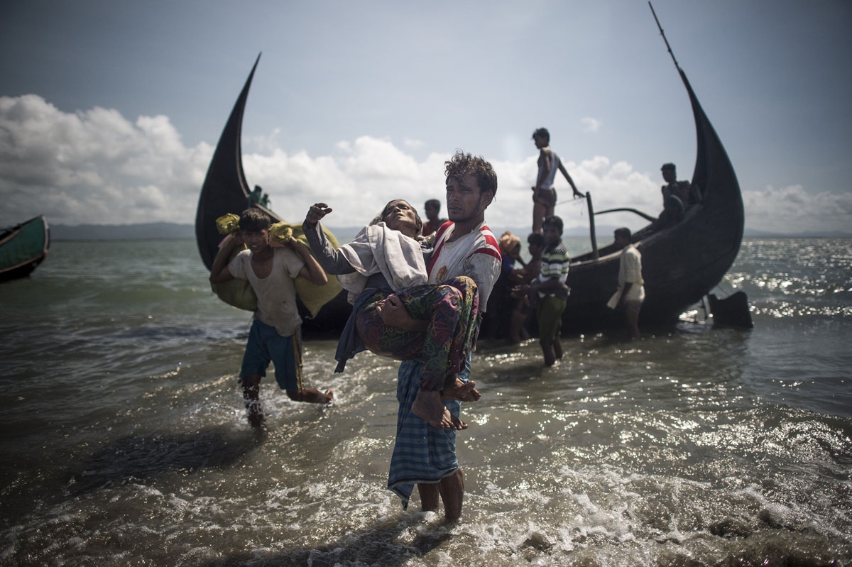 A Bangladeshi man helps Rohingya Muslim refugees to disembark from a boat on the Bangladeshi shoreline of the Naf river after crossing the border from Myanmar in Teknaf on September 30, 2017.