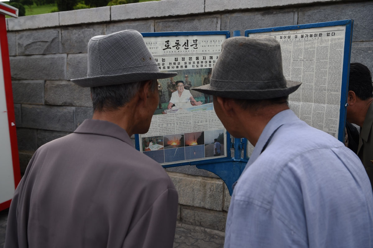 Two men read a copy of the Rodong Sinmun newspaper showing coverage of North Korean leader Kim Jong-Un overseeing a ballistic missile test conducted by the Hwasong artillery units of the KPA Strategic Force, in a public square in Pyongyang on July 20, 201