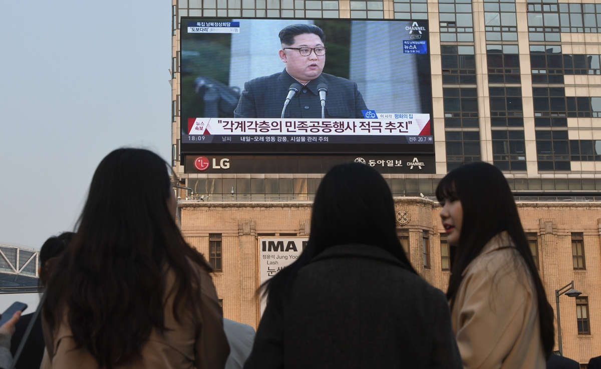 Pedestrians walk cross the road as a big screen shows live footage of a joint press conference between South Korean President Moon Jae-in and North Korean leader Kim Jong Un during the inter-Korean summit, in downtown Seoul on April 27, 2018.
