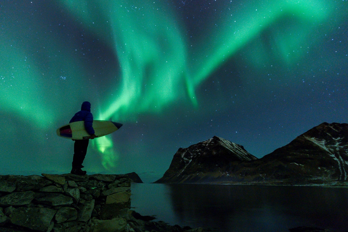 A surfer looks at Northern Lights on March 9, 2018 in Utakleiv, northern Norway, Lofoten islands, within the Arctic Circle.
