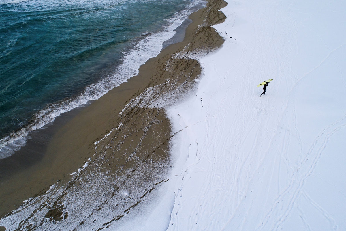 A surfer carries his surfboard as he walks through the snow out of the water on March 11, 2018 in Unstad, northern Norway, Lofoten islands, within the Arctic Circle as air temperature drops minus 13°C and water temperature above 4°C. / A