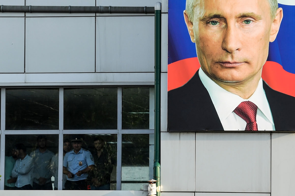 People look out of a window at Grozny Airport adorned with a portrait of Russian President Vladimir Putin in Grozny, on July 24, 2017.