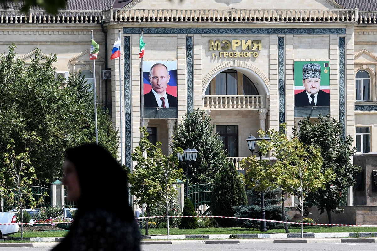 A woman walks on an avenue named after Russian President Vladimir Putin in front of the Grozny city administration's building displaying portraits of Russian President Vladimir Putin (L) and Akhmad Kadyrov (R), former Chechen Republic's president and fath