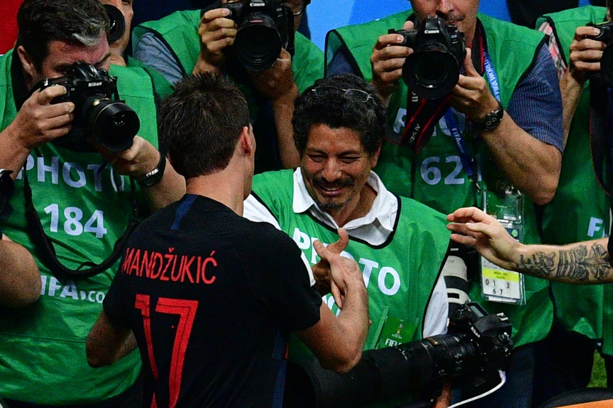 Croatia's forward Mario Mandzukic (L) shakes hands with AFP photographer Yuri Cortez (C) after falling on him with teammates while celebrating their second goal during the Russia 2018 World Cup semi-final football match between Croatia and England at the