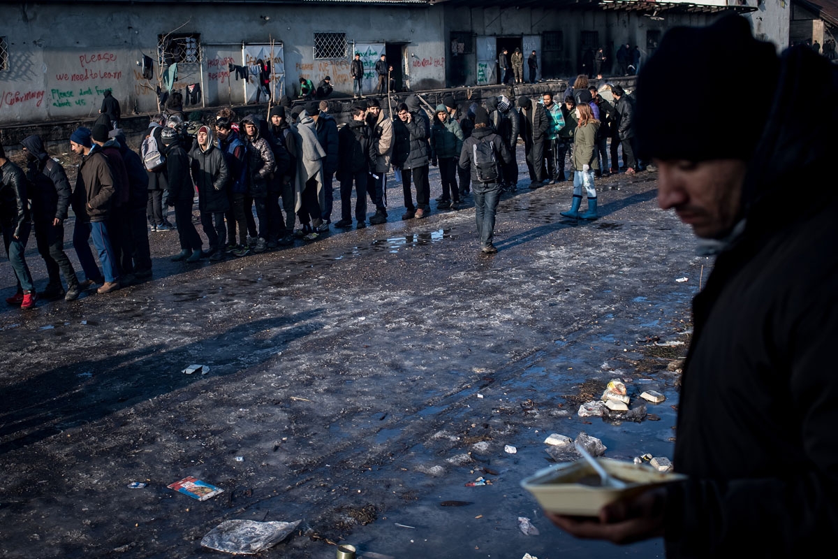 Migrants stand in line for food distributed by volunteers outside of derelict warehouses which they use as a makeshift shelter, in Belgrade on January 15, 2017, with temperatures just bellow zero Celsius overnight.