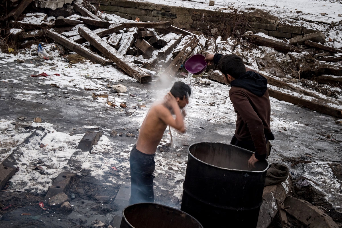 A migrant washes himself outside a derelict warehouse used as a shelter near Belgrade's main railway station on January , 2017, with temperatures bellow zero Celsius.