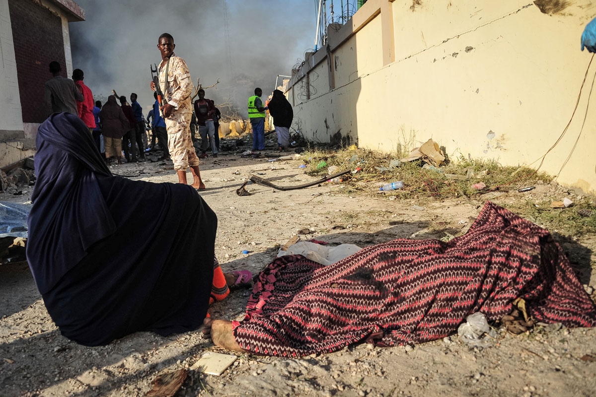 a woman sits by the body of a victim at the site of the explosion of a truck bomb in the centre of Mogadishu, on October 14, 2017.