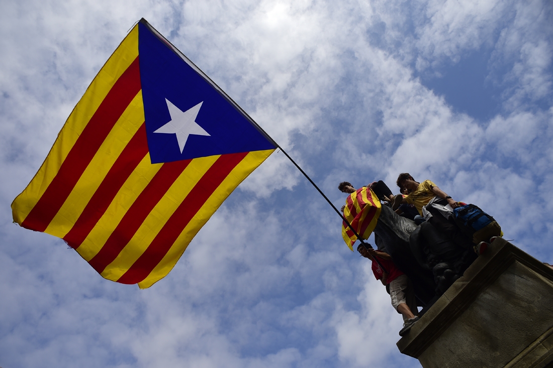 Protesters wave a giant Catalan pro-independence 'Estelada' flag atop a sculpture during a demonstration in Barcelona on October 2, 2017 a day after hundreds were injured in a police crackdown during Catalonia's banned independence referendum.