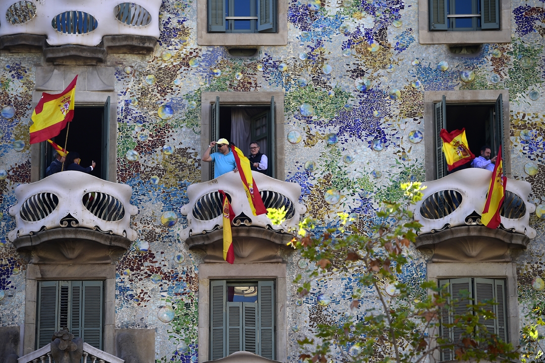 People wave Spanish flags from the Casa Batllo during a pro-unity demonstration in Barcelona on October 29, 2017. Pro-unity protesters were to gather in Catalonia's capital Barcelona, two days after lawmakers voted to split the wealthy re