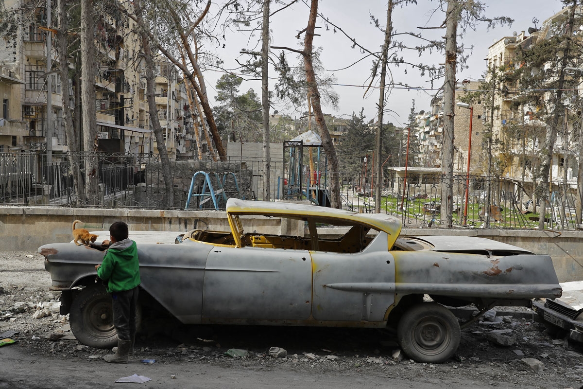 A picture taken on March 9, 2017, shows a boy playing with a cat next to a 1948 Buick parked outside the home of Mohammad Mohiedine Anis in the formerly rebel-held al-Shaar neighbourhood.