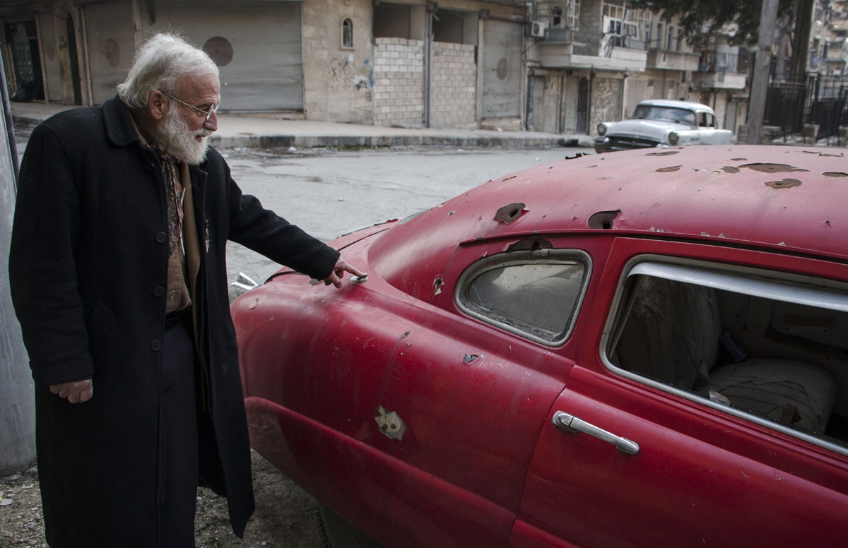 Abu Omar a 69-year-old Syrian classic car collector, gestures towards bullet holes on one of his cars in the rebel held al-Shaar district of the northern Syrian city of Aleppo, on December 20, 2015.