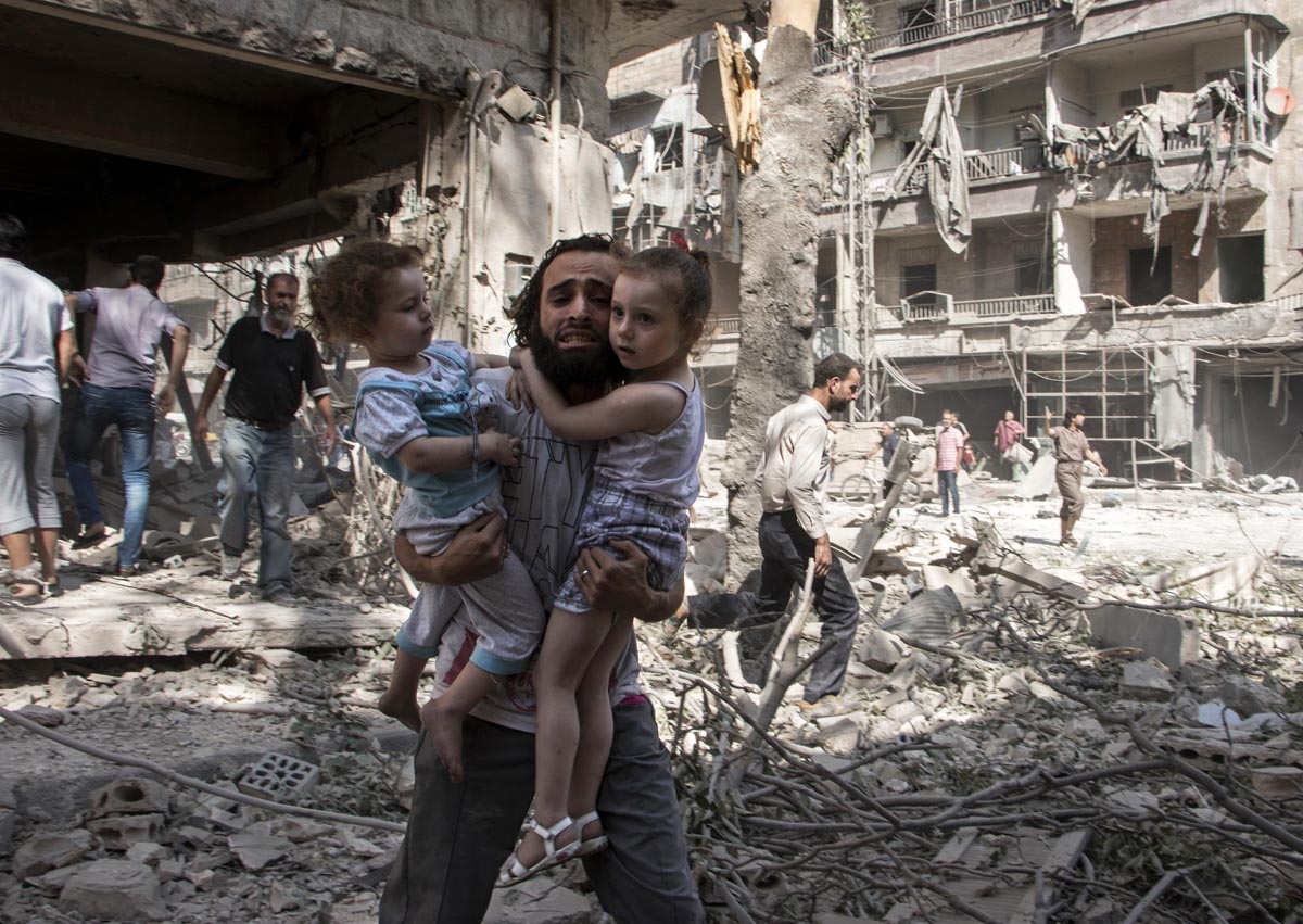 A Syrian man carries his two girls as he walks across the rubble following a barrel bomb attack on the rebel-held neighbourhood of al-Kalasa in the northern Syrian city of Aleppo on September 17, 2015