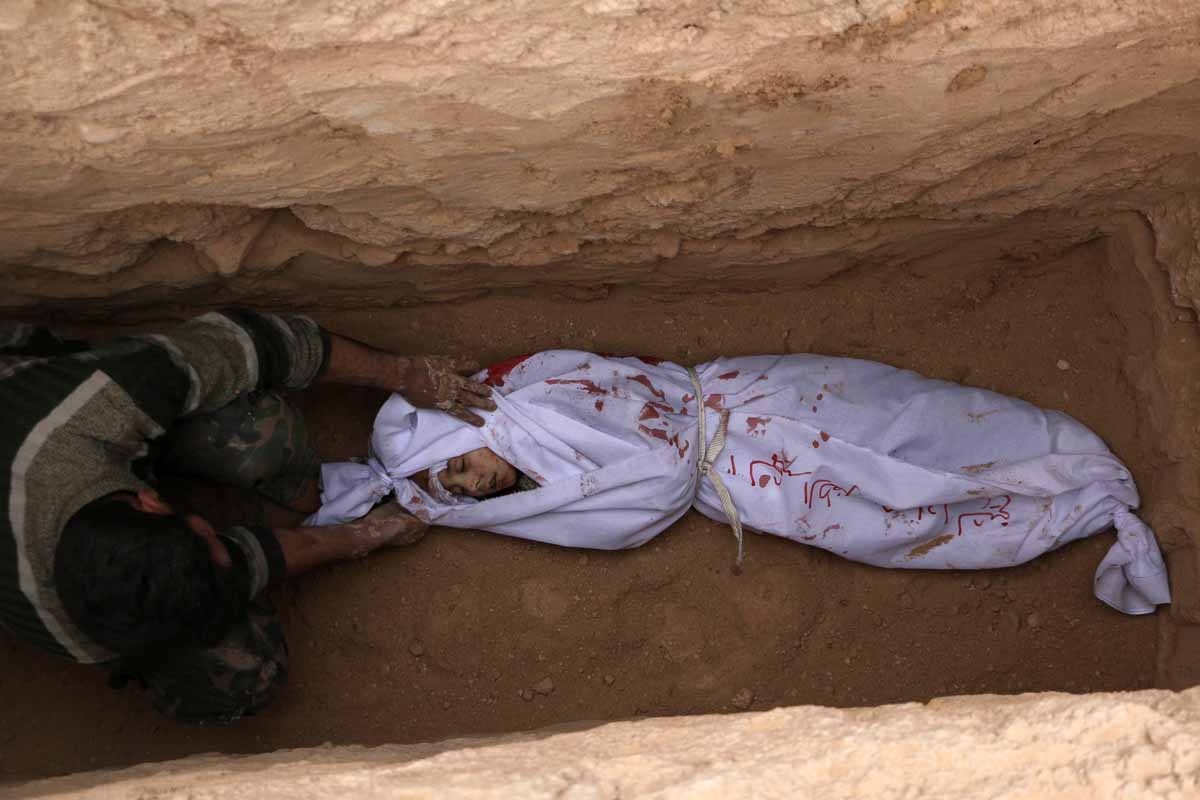 A Syrian places the body of a child in a grave during a group funeral ceremony at a cemetery following reported airstrikes on January 7, 2016 in the rebel-held city of Douma, northeast of the capital Damascus. A Syrian places the body of a child in a grave during a group funeral ceremony at a cemetery following reported airstrikes on January 7, 2016 in the rebel-held city of Douma, northeast of the capital Damascus.