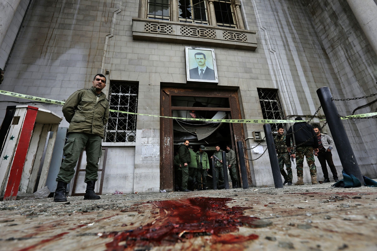 Syrian security forces gather under a portrait of President Bashar al-Assad at the old palace of justice building in Damascus following a reported suicide bombing on March 15, 2017. Two suicide bombings hit Damascus including the attack at the central cou