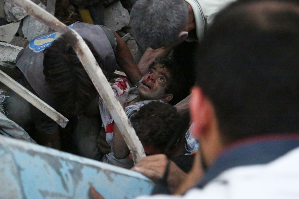 Syrians evacuate an injured boy from rubble following a reported air strike on a rebel-held town of Douma, northeast of the capital Damascus on June 16, 2015.