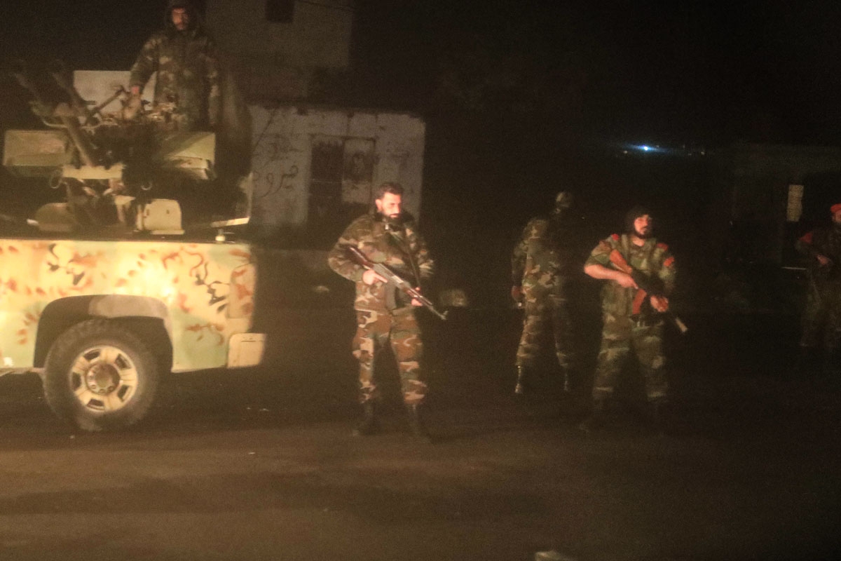 A picture taken through a window of a bus carrying Syrian civilians and rebel-fighters from the town of Douma shows pro-government forces standing guard at a checkpoint in the city of Tartus, on April 2, 2018.