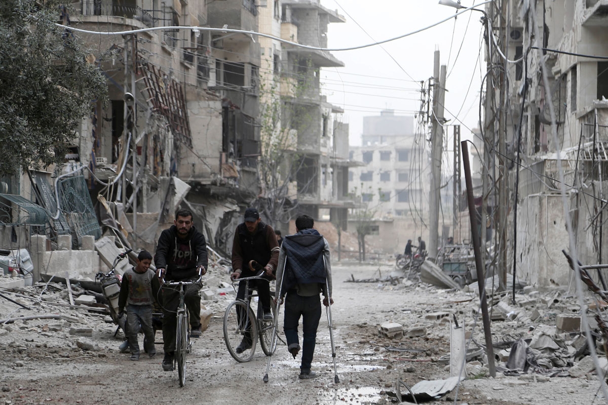 Syrian people walk down a destroyed street as civilians and rebels prepare to evacuate one of the few remaining rebel-held pockets in Zamalka, in Eastern Ghouta, on the outskirts of the Syrian capital Damascus, on March 24, 2018. Syrian rebels and civilia