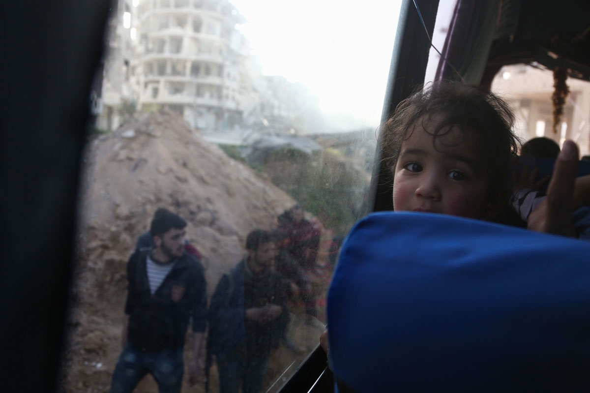 A convoy transporting Syrian civilians and rebel fighters drives past destroyed buildings in Arbin in Eastern Ghouta as they are evacuated from the opposition enclave to the village of Qalaat al-Madiq, some 45 kilometres northwest of the central city of H