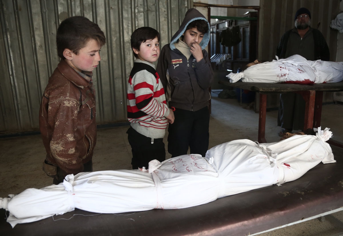 Children stand over the body of a child at a makeshift hospital, following an airstrike in the rebel-held besieged town of Arbin, in the eastern Ghouta region on the outskirts of the capital Damascus on February 2, 2018.
