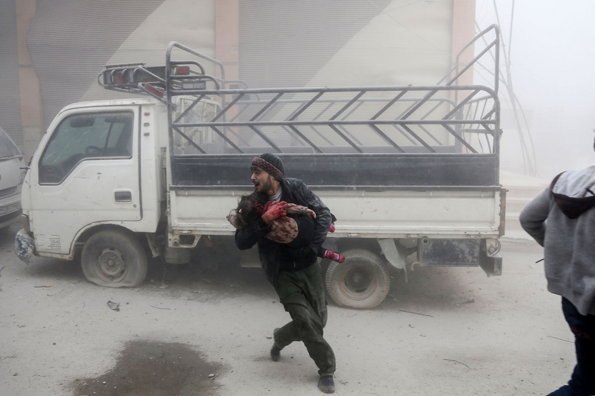 / A man carries a child as he flees from reported Syrian air force strikes that hit the rebel-held town of Saqba, in the besieged Eastern Ghouta region on the outskirts of the capital Damascus, on February 6, 2018.