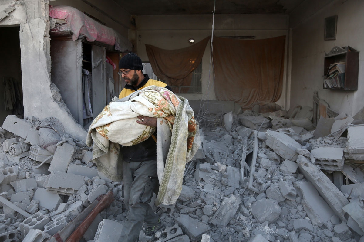 A member of the Syrian civil defence carries the body of a child out of the rubble of a house that was hit by a reported regime air strike in the rebel-held town of Jisreen, in the besieged Eastern Ghouta region on the outskirts of the capital Damascus, o