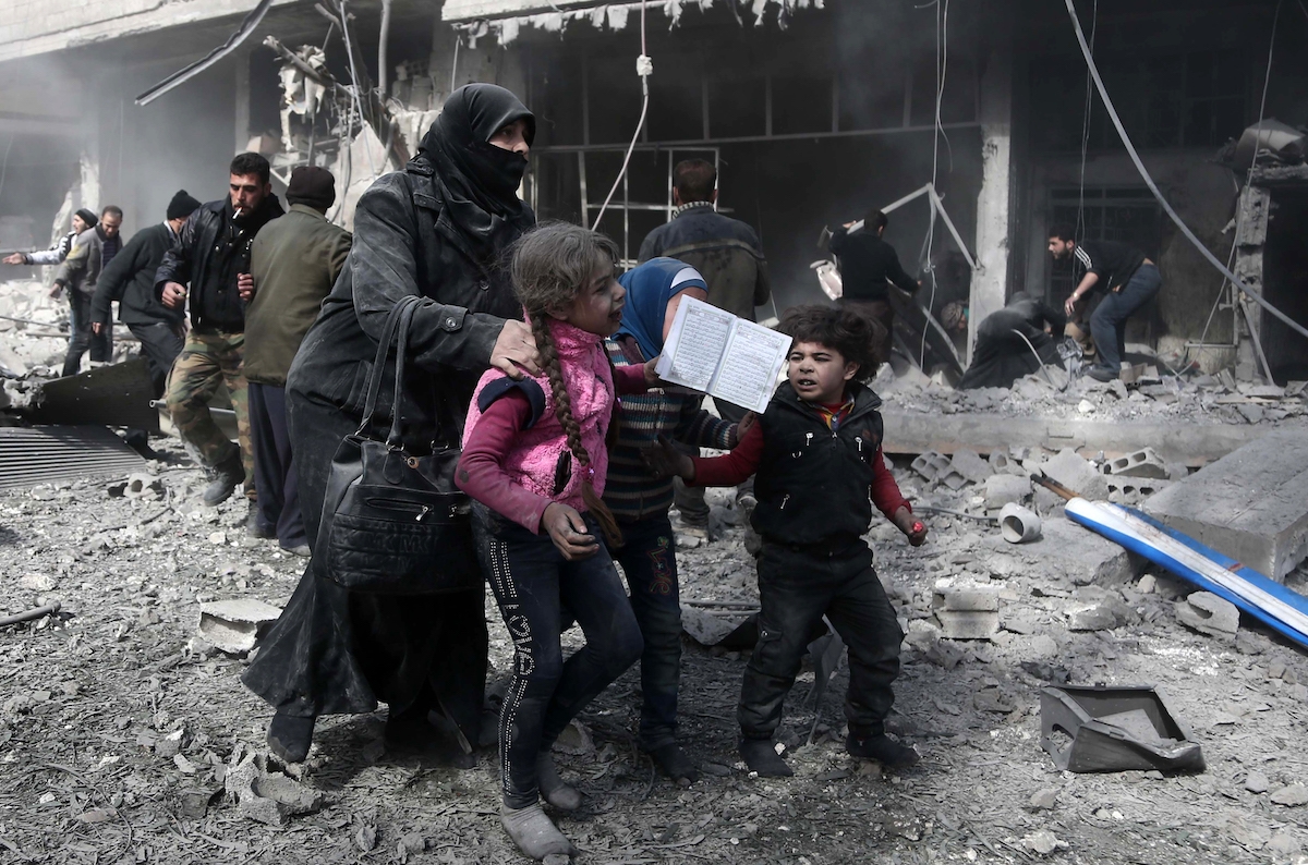 A Syrian woman and children run for cover amid the rubble of buildings following government bombing in the rebel-held town of Hamouria, in the besieged Eastern Ghouta region on the outskirts of the capital Damascus, on February 19, 2018.