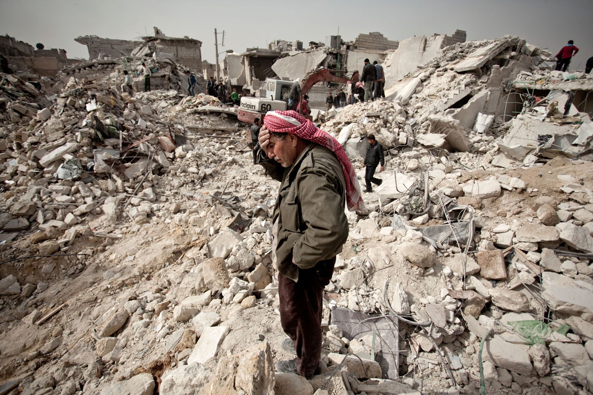 A Syrian man reacts while standing on the rubble of his house while others look for survivors and bodies in the Tariq al-Bab district of the northern city of Aleppo on February 23, 2013.
