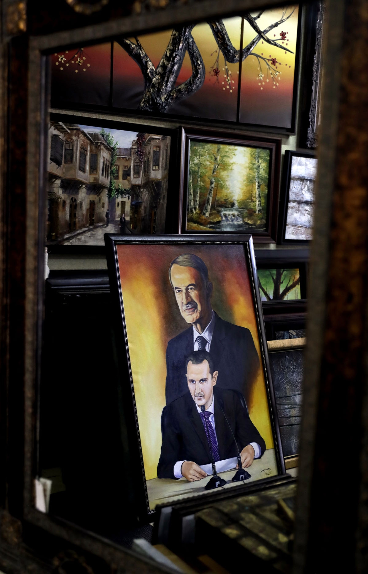 An oil painting depicting a portrait of Syrian President Bashar al-Assad and his late father Hafez al-Assad are seen at an art gallery in the capital Damascus on July 3, 2017. / AFP PHOTO / Joseph EID