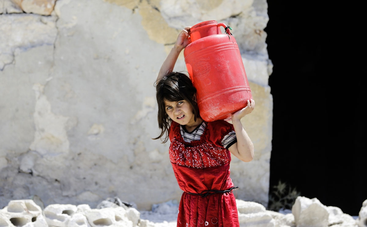 A Syrian girl carries a large jug of water on her back while on her way home, in the Kallaseh district of the northern city of Aleppo, on July 5, 2017.
