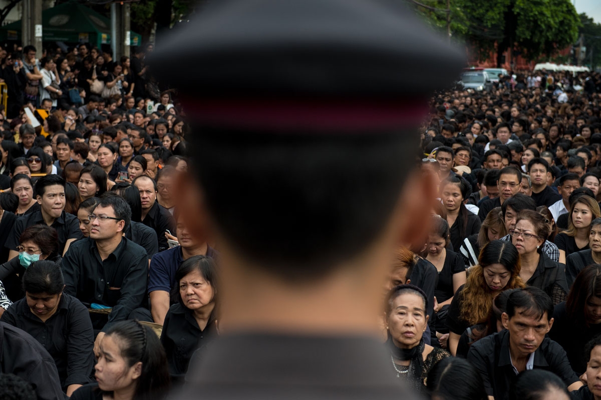 A large crowd clad in black who came to pray for the late Thai King Bhumibol Adulyadej is watched by a Thai policeman in front of the Grand Palace in Bangkok on October 16, 2016.
