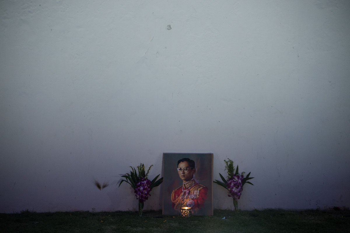 A lit candle and flowers adorn an image of the late Thai King Bhumibol Adulyadej on the outer wall of the Grand Palace at dawn on October 16, 2016.