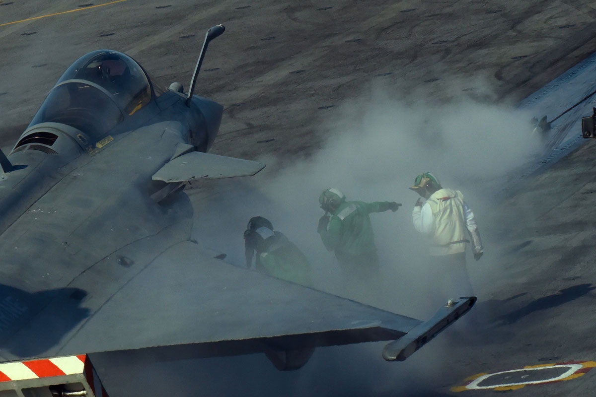 The steam from the aircraft catapult engulfs ordnance men and a security officer (white jacket) as a French Rafale jet gets ready to take off from the deck of the USS George H.W. Bush aircraft carrier on May 11, 2018 in the Atlantic Ocean.