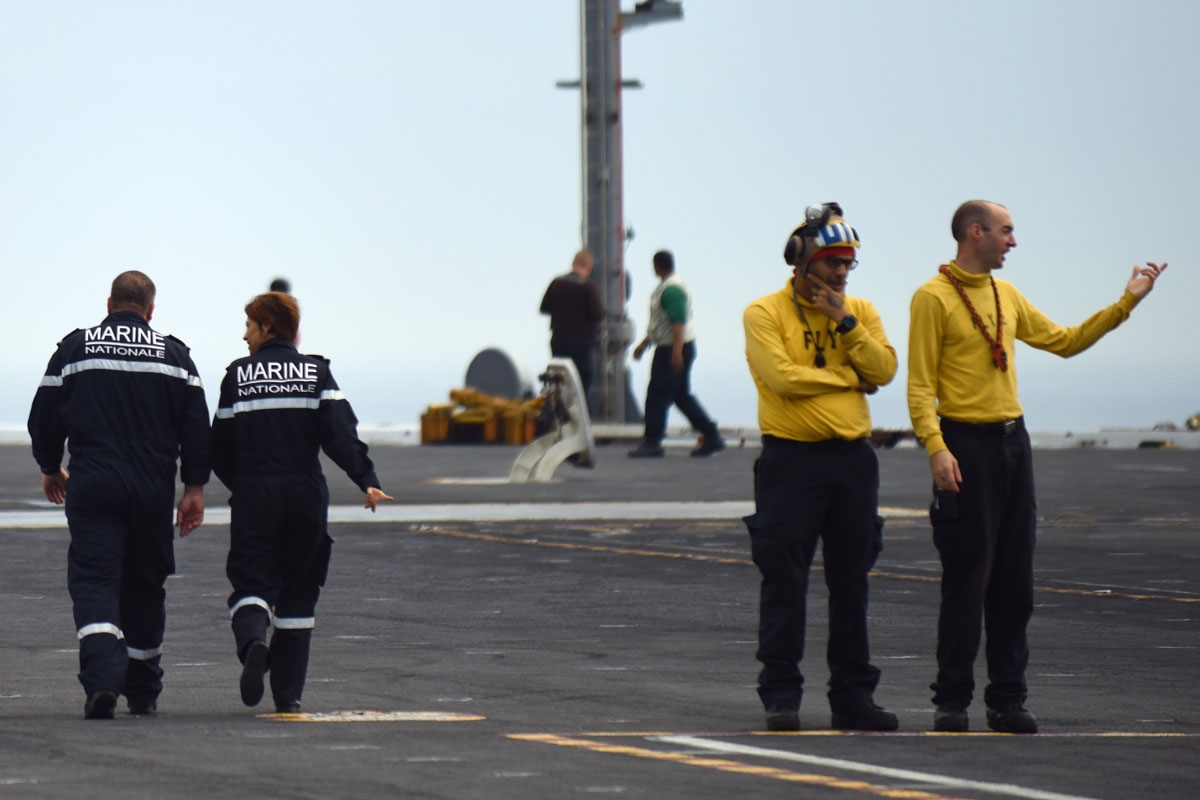 French Navy personnel (L) walk past US catapult officers on the deck of the USS George H.W. Bush aircraft carrier on May 12, 2018 in the Atlantic Ocean.