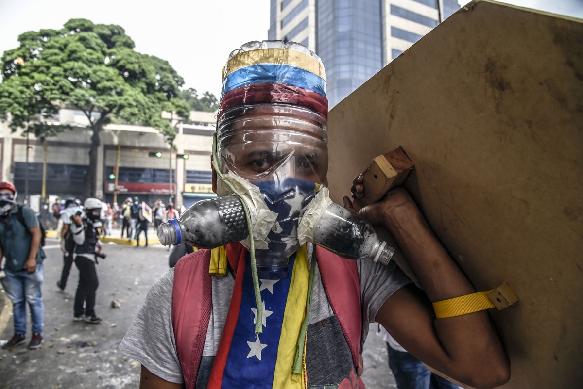 A Venezuelan opposition activist wearing a homemade gas mask takes cover behind a makeshift shield as clashes erupt with riot police during a protest against President Nicolas Maduro, in Caracas on May 8, 2017.