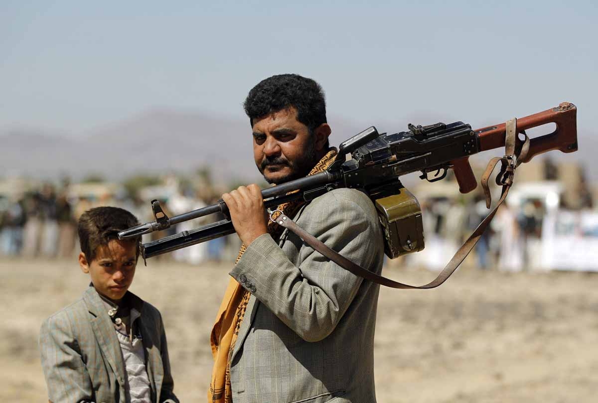 A Yemeni Huthi fighter carrying his weapon stands next to a child during a gathering to mobilise more fighters into several battlefronts on November 1 ,2016 on the outskirts of the capital Sanaa.