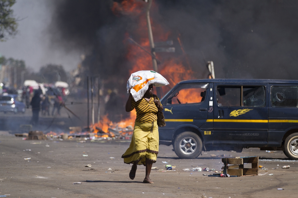 A woman carrying groceries on her head runs away as Zimbabwe's opposition supporters set up a burning barricade as they clash with police during a protest for electoral reforms on August 26, 2016 in Harare, Zimbabwe.
