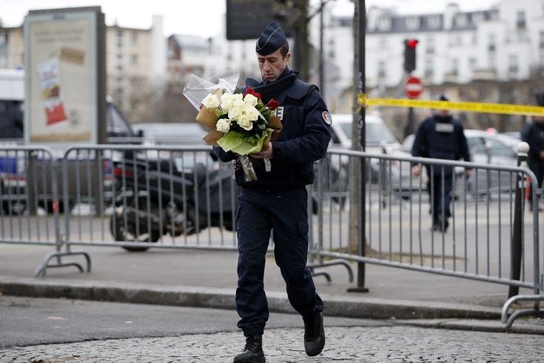 Un policier va poser devant l'épicerie des fleurs apportées par des passants au lendemain de l'attaque Un policier va poser devant l'épicerie des fleurs apportées par des passants au lendemain de l'attaque