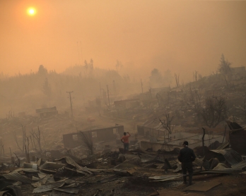 People walk amid the remains of burnt down buildings after a forest fire in Santa Olga, 240 kilometres south of Santiago, on January 26, 2017. 