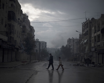 A father and son return home with vegetables, as smoke from a pro-government forces artillery strike ascends in the background, in the al-Amaria neighbourhoodin the city of Aleppo, on January 6, 2013.  