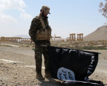 Un membre des forces pro-gouvernementales syriennes porte un drapeau du groupe Etat islamique découvert après la reprise de Palmyre, le 27 mars 2016 (AFP)